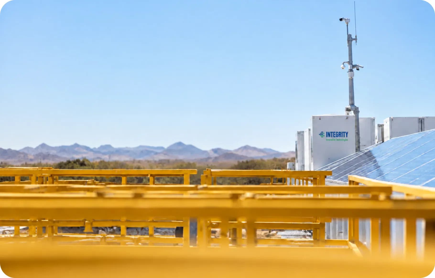 A yellow site guardrail in the foreground with battery cabinets and mountains beyond